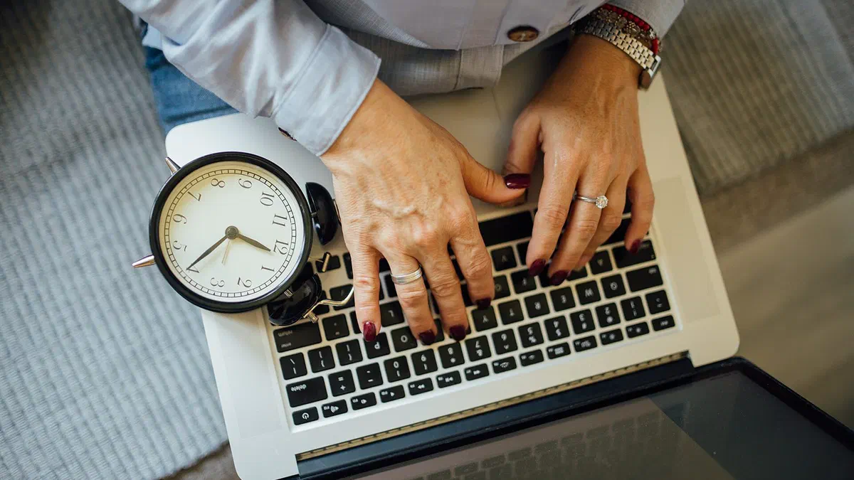 Mains tapant sur le clavier d'un ordinateur portable, à côté d'un réveil